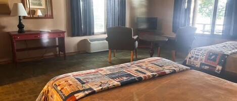 A hotel room with a large bed, a desk, a chair, a television, and two windows with curtains.