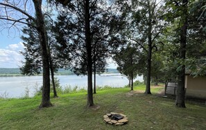 Une propriété au bord du lac, dotée d’un foyer extérieur, d’arbres et offrant une vue sur le lac.