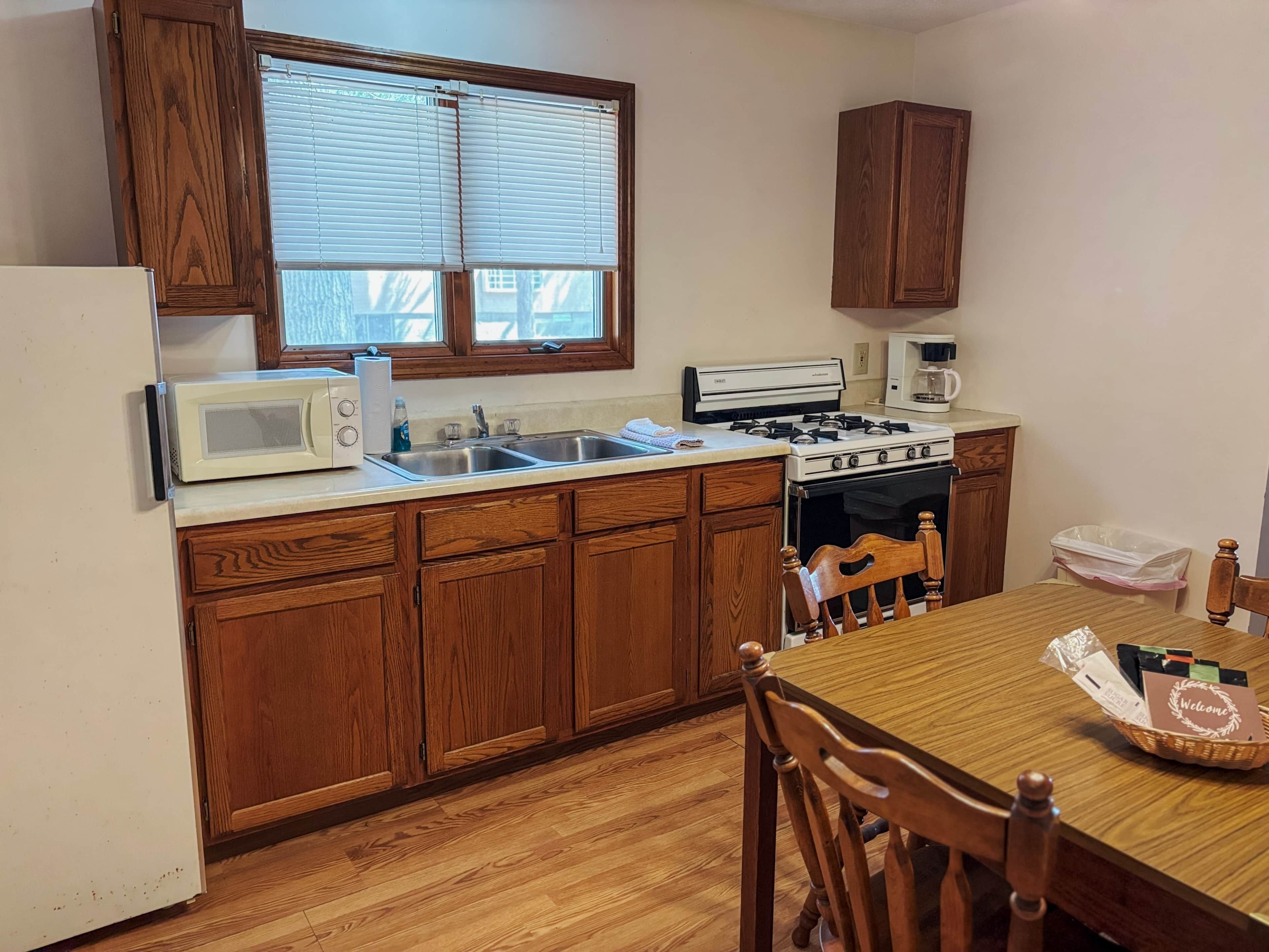 A kitchen with wooden cabinets, a microwave, stove, sink, and a dining table with chairs.