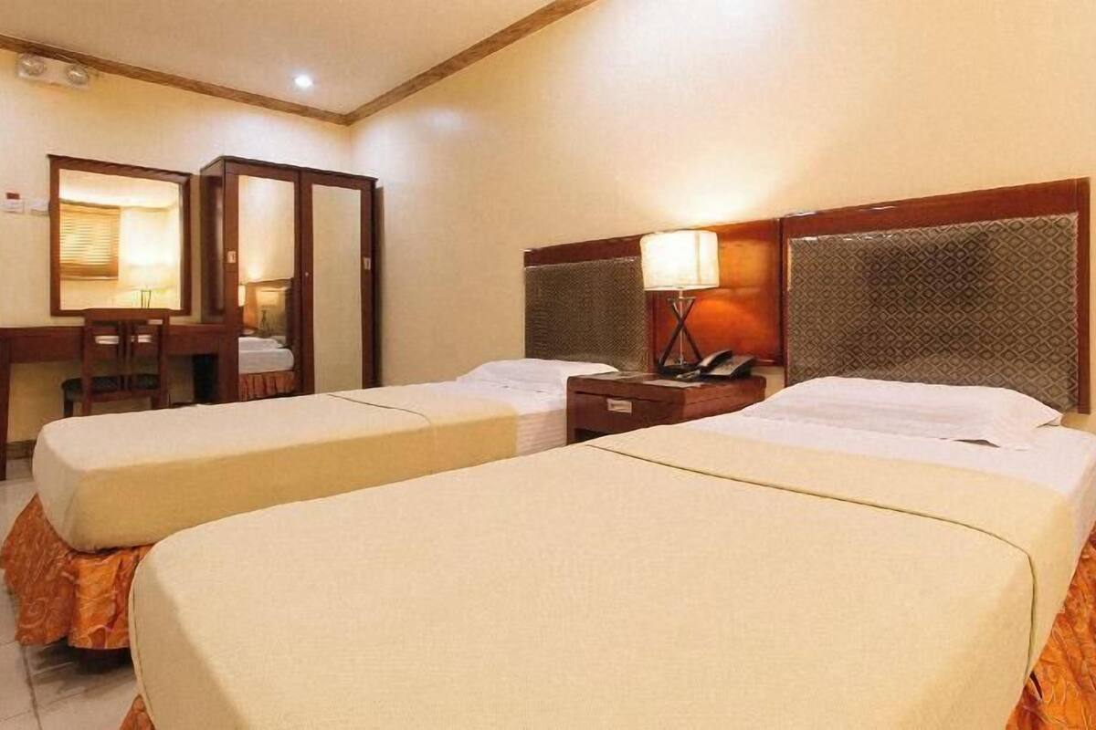 Una habitación de hotel con dos camas, un escritorio, una silla y un espejo.