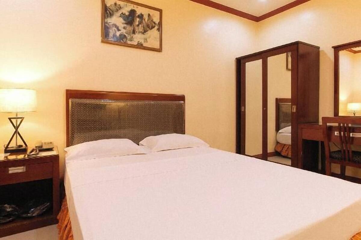 Una habitación de hotel con cama, mesita de noche, lámpara y espejo.