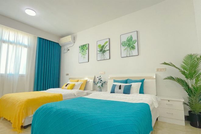 A hotel room with two beds, each with a different colored bedspread, a large potted plant, and three framed plant illustrations on the wall.