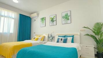 A hotel room with two beds, each with a different colored bedspread, a large potted plant, and three framed plant illustrations on the wall.