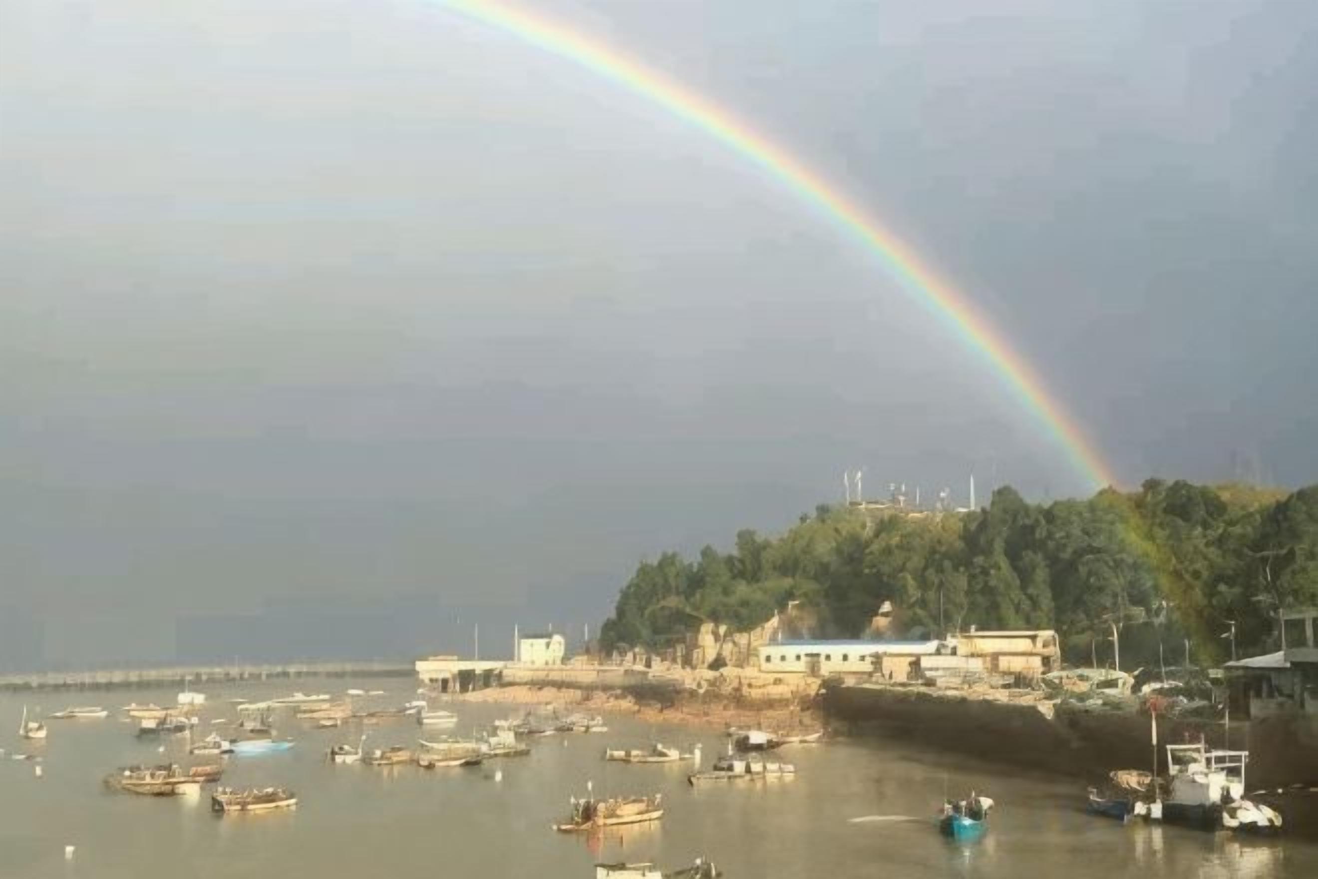 A coastal scene with boats, a rainbow, and buildings along the shore.