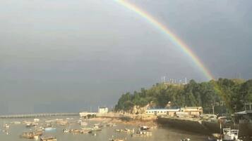 A coastal scene with boats, a rainbow, and buildings along the shore.