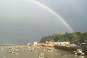 Eine Küstenlandschaft mit Booten, einem Regenbogen und Gebäuden am Ufer.