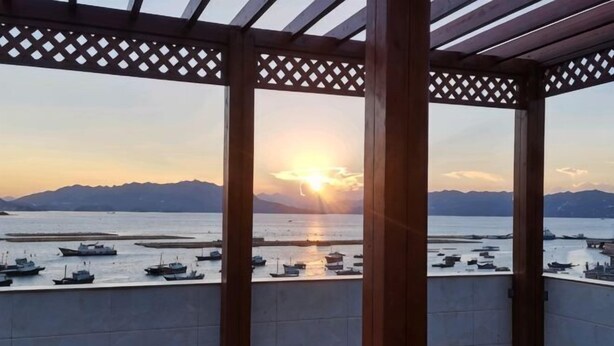A covered balcony with a view of boats on a body of water and mountains in the distance.