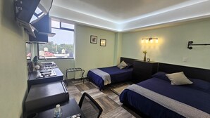 Une chambre d’hôtel avec deux lits, un bureau équipé d’une cuisinière à gaz, une chaise et une petite table sur laquelle se trouvent une bouteille et une télécommande.