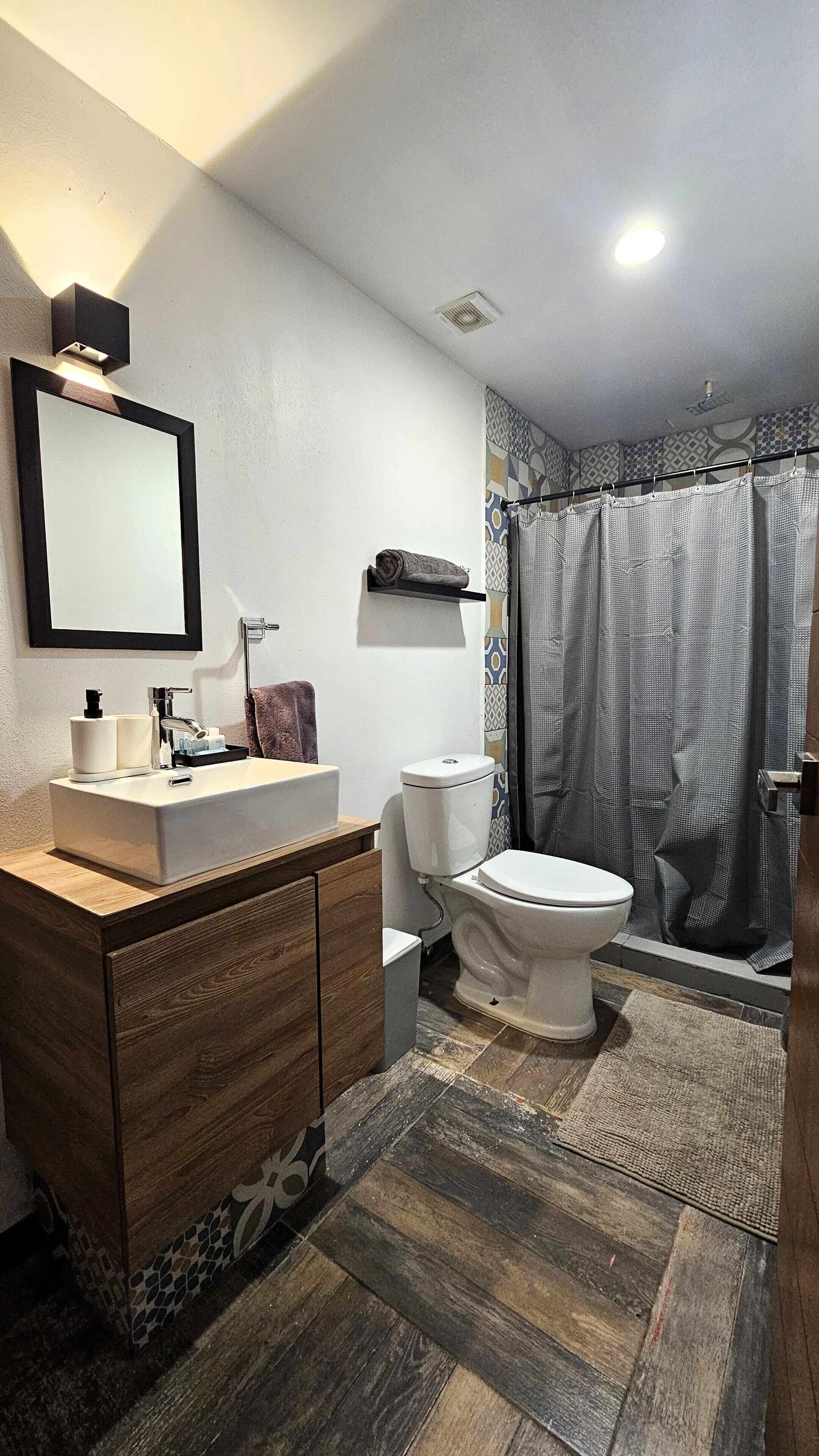 A bathroom with a wooden vanity, a white sink, a toilet, and a shower curtain.