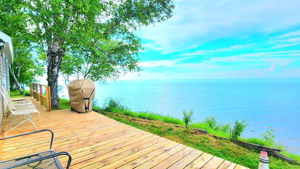 Une terrasse en bois dotée d’un barbecue couvert, de coins salon extérieurs et offrant une vue sur l’eau.
