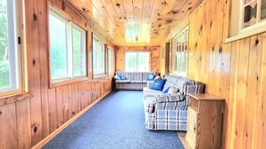 L’intérieur d’une cabane, avec un long couloir, des murs en bois, une moquette bleue et un canapé à carreaux agrémenté de coussins.
