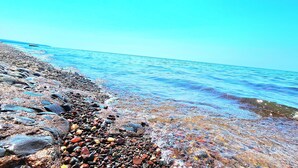 Une plage rocheuse bordée d’une eau d’un bleu limpide et surplombée d’un ciel dégagé.