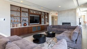 A modern living room with a sectional sofa, a flat-screen TV, and a built-in entertainment unit with shelves and cabinets. - Pentagon Luxe Apartments (Arlington)