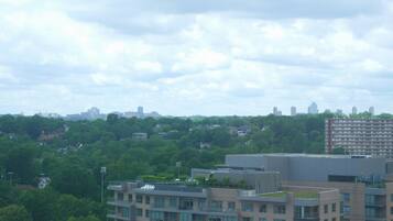 A multi-story building with a flat roof and large windows, surrounded by greenery and other buildings in the background.