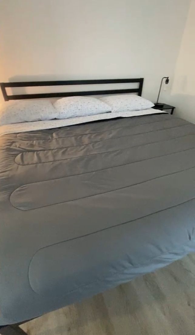 A bed with a grey mattress and a black metal frame.