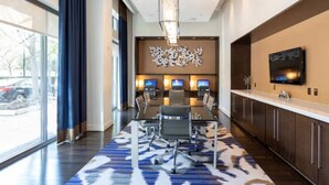 A modern hotel lobby with a large conference table, multiple computer stations, and a large TV screen on the wall. - Pentagon Luxe Apartments (Arlington)