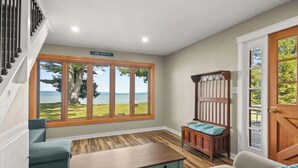 A room with a large window overlooking a lake, a wooden bench, a sofa, and a staircase. - Torch Ever Blue | SandBar | Waterfront (Rapid City)