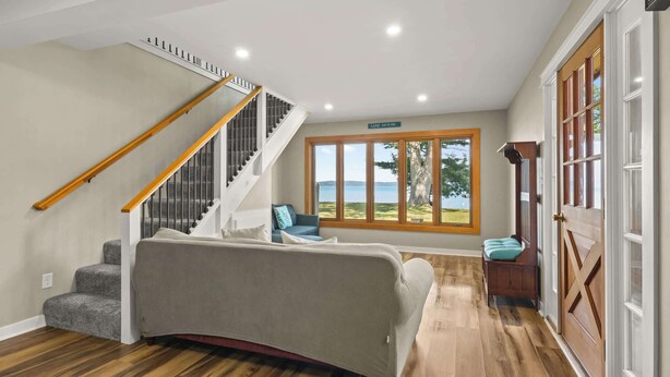 A spacious room with a large window offering a view of the outdoors, a staircase with a wooden handrail, and a cozy seating area with a sofa and a bench. - Torch Ever Blue | SandBar | Waterfront (Rapid City)