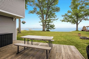 Une terrasse en bois avec une table de pique-nique, un pot de fleurs suspendu et une vue sur la mer.