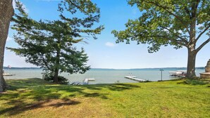 A grassy area with a dock extending into a lake, surrounded by trees. - Torch Ever Blue | SandBar | Waterfront (Rapid City)