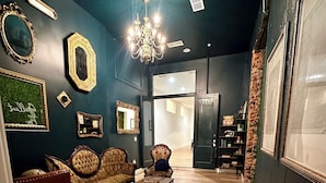 A modern living room with a dark wall, a chandelier, a sofa, a coffee table, and a cowhide rug. - Gallant Fox - NuLu/Downtown (Louisville)