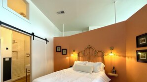 A bedroom with a large bed, a wooden floor, a white wall, and a picture of a person on the wall. - Gallant Fox - NuLu/Downtown (Louisville)