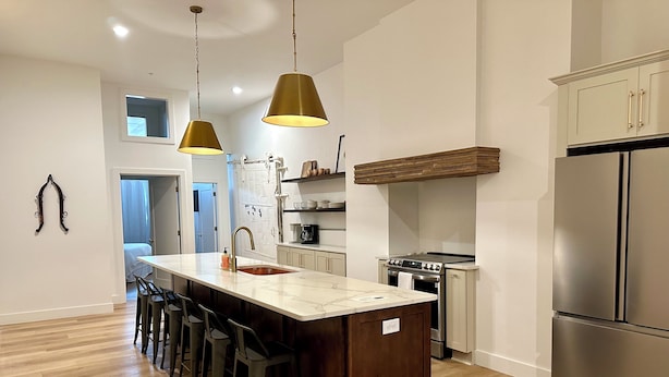 A modern kitchen with a central island, bar stools, stainless steel appliances, and pendant lighting. - Gallant Fox - NuLu/Downtown (Louisville)