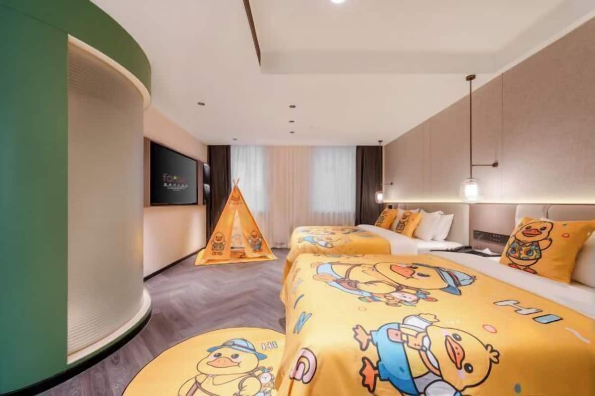 Habitación de hotel con dos camas, una pared de acento verde, un televisor de pantalla plana y una decoración tipo tienda de campaña.