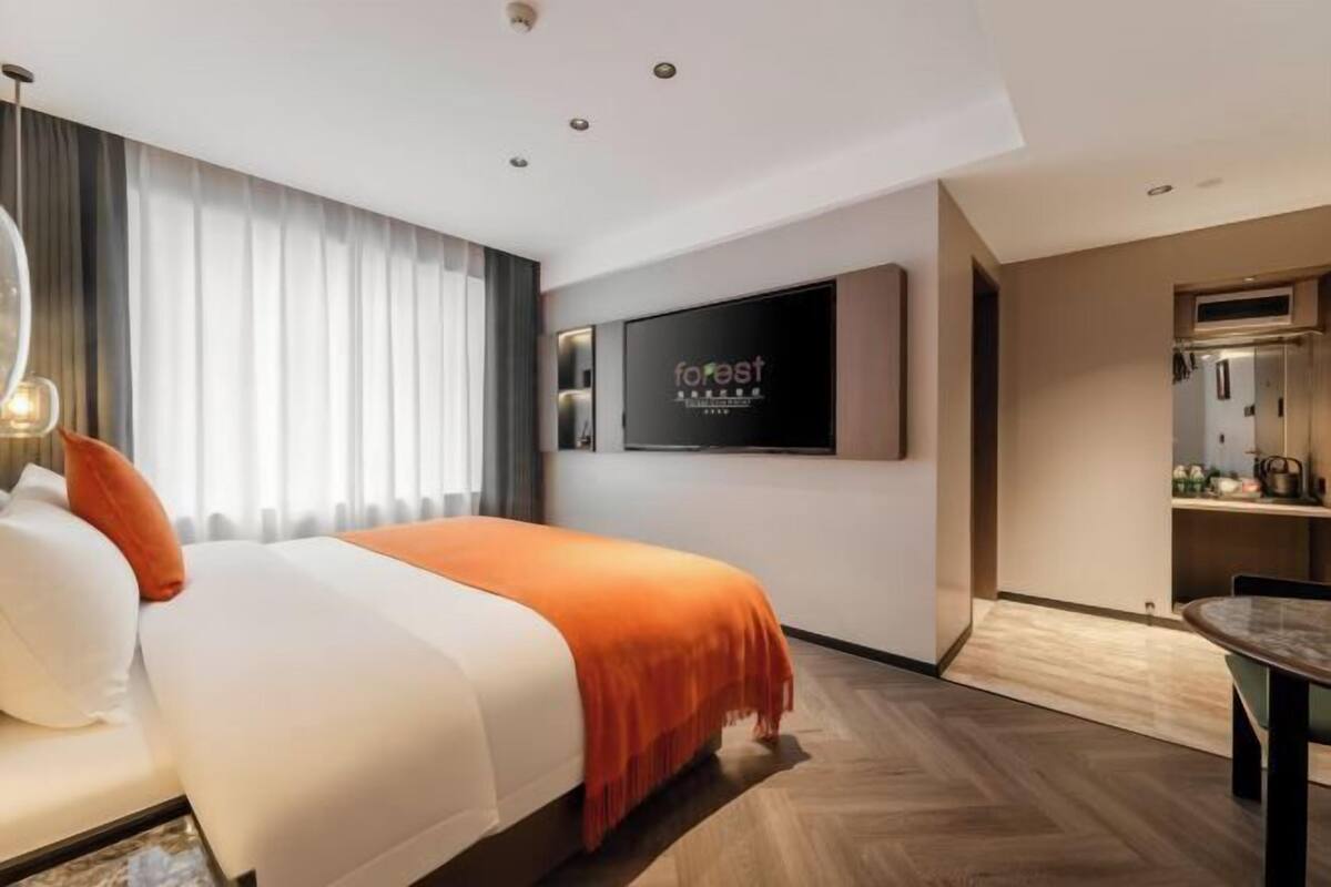 Una habitación de hotel moderna con una cama, un televisor montado en la pared y una zona de comedor.