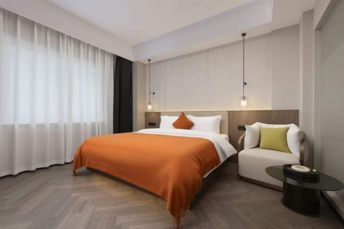 Una habitación de hotel moderna con una cama grande, un sofá, una mesita y una ventana con cortinas.