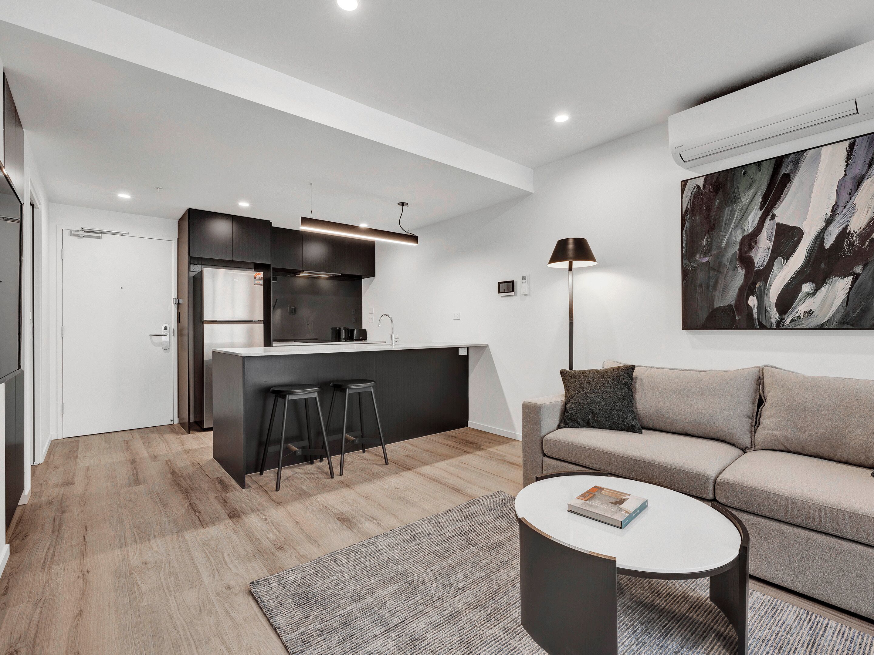 A modern living room with a sofa, a coffee table, and a kitchen area with stools.