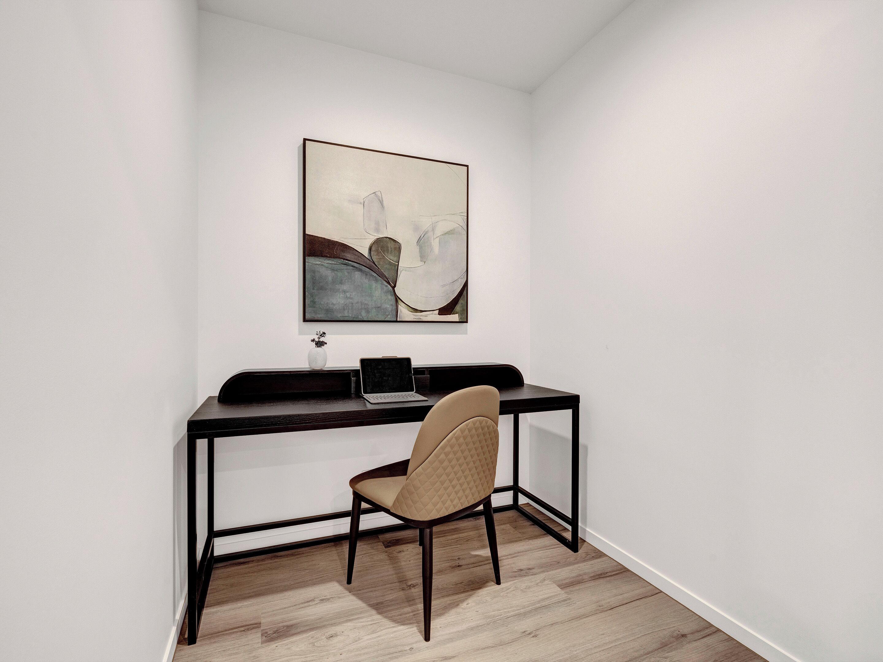 Una habitación de esquina con escritorio, silla y un cuadro en la pared.