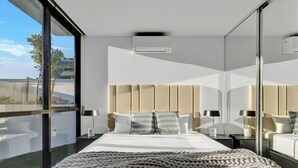 Una habitación de hotel moderna con una cama grande, dos mesitas de noche, un ventanal amplio y un equipo de aire acondicionado.