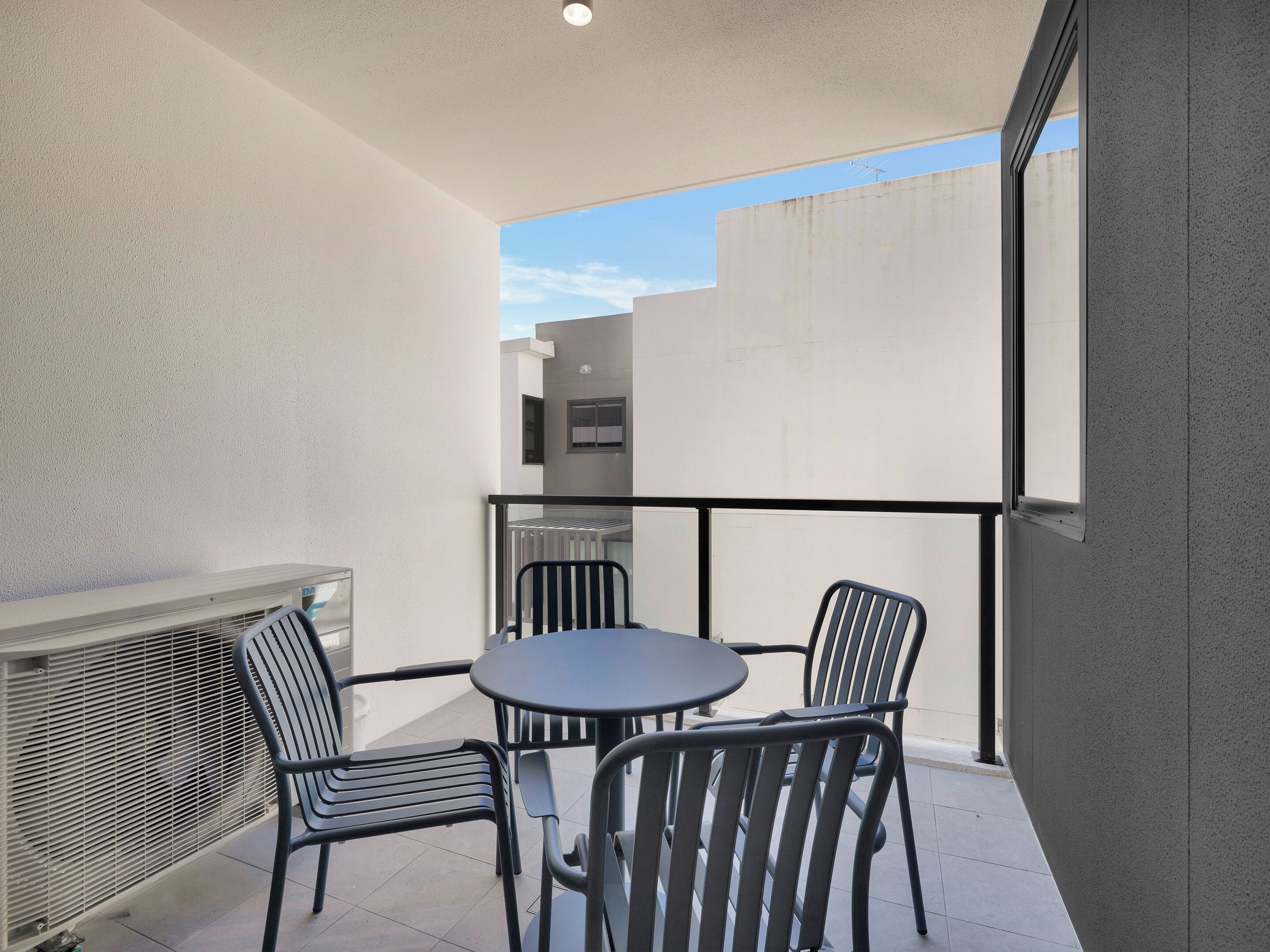 En balkon med et bord og stole, en radiator og udsigt til bygninger.