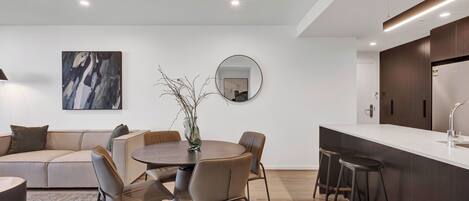 A modern living room with a round dining table, a sofa, and a kitchen area with a bar counter.
