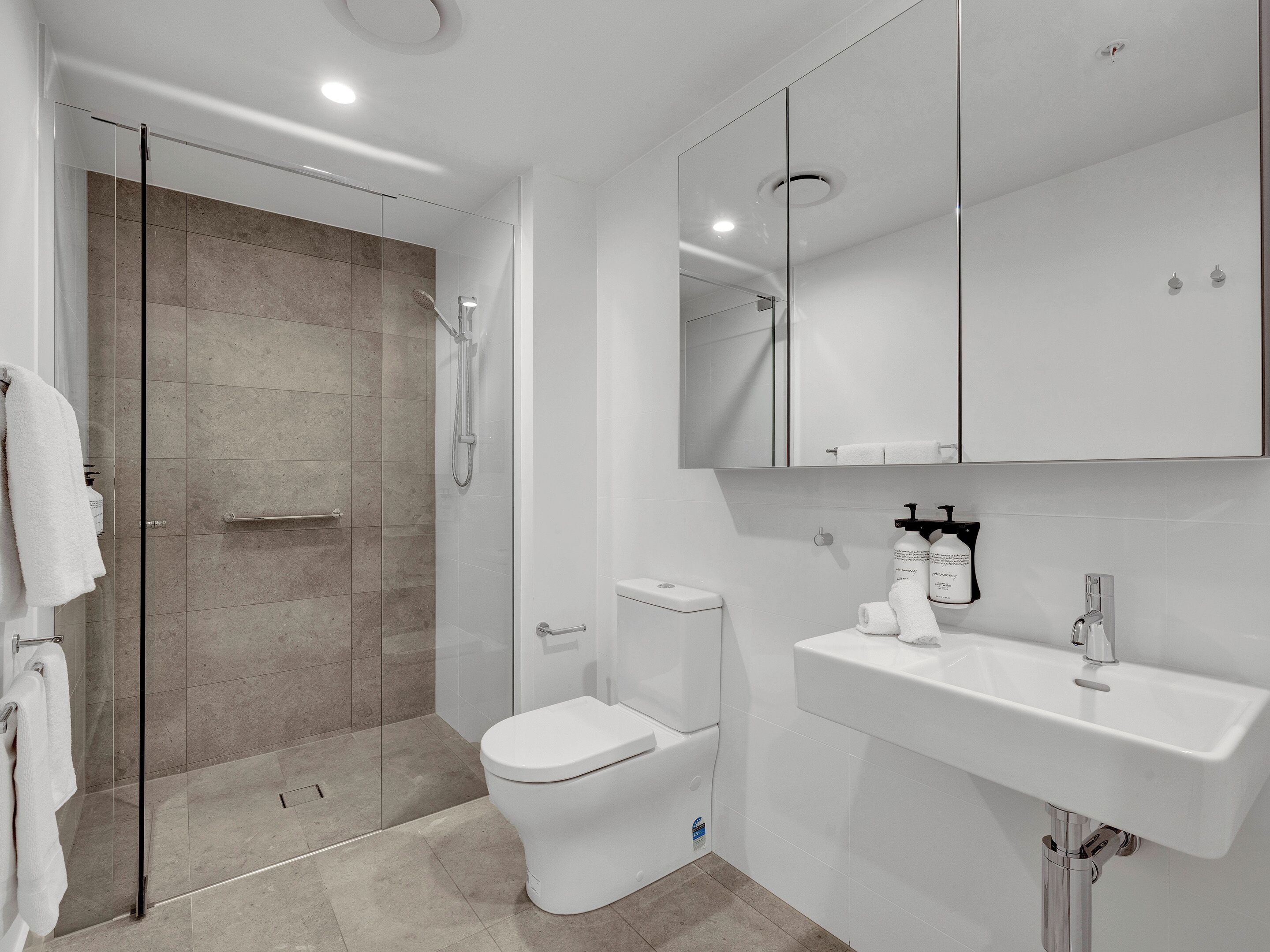 A modern bathroom with a glass-enclosed shower, a white toilet, and a white sink with a mirror above it.