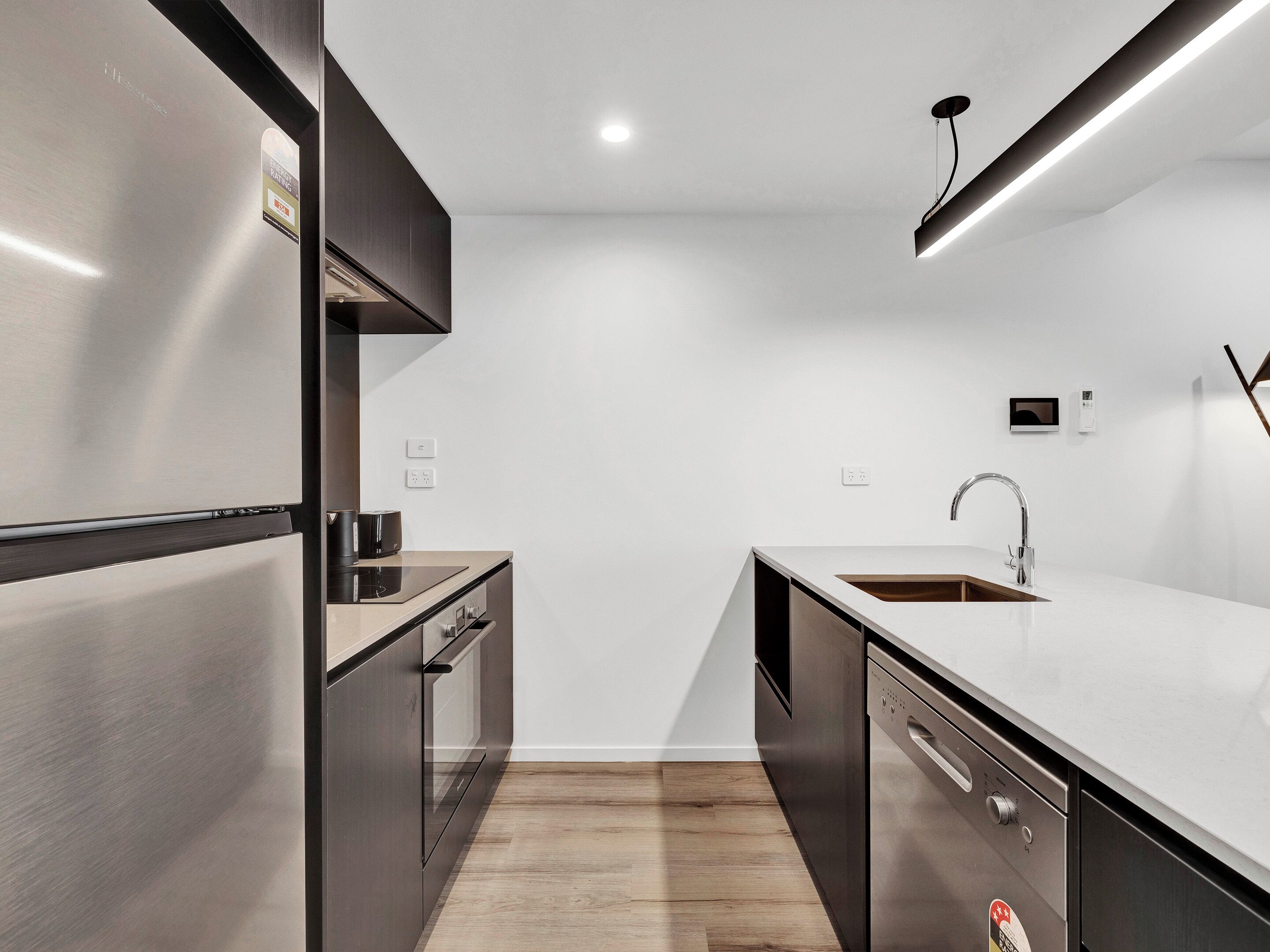 A modern kitchen with stainless steel appliances, a wooden floor, and a minimalist design.