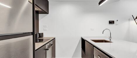 A modern kitchen with stainless steel appliances, a wooden floor, and a minimalist design.