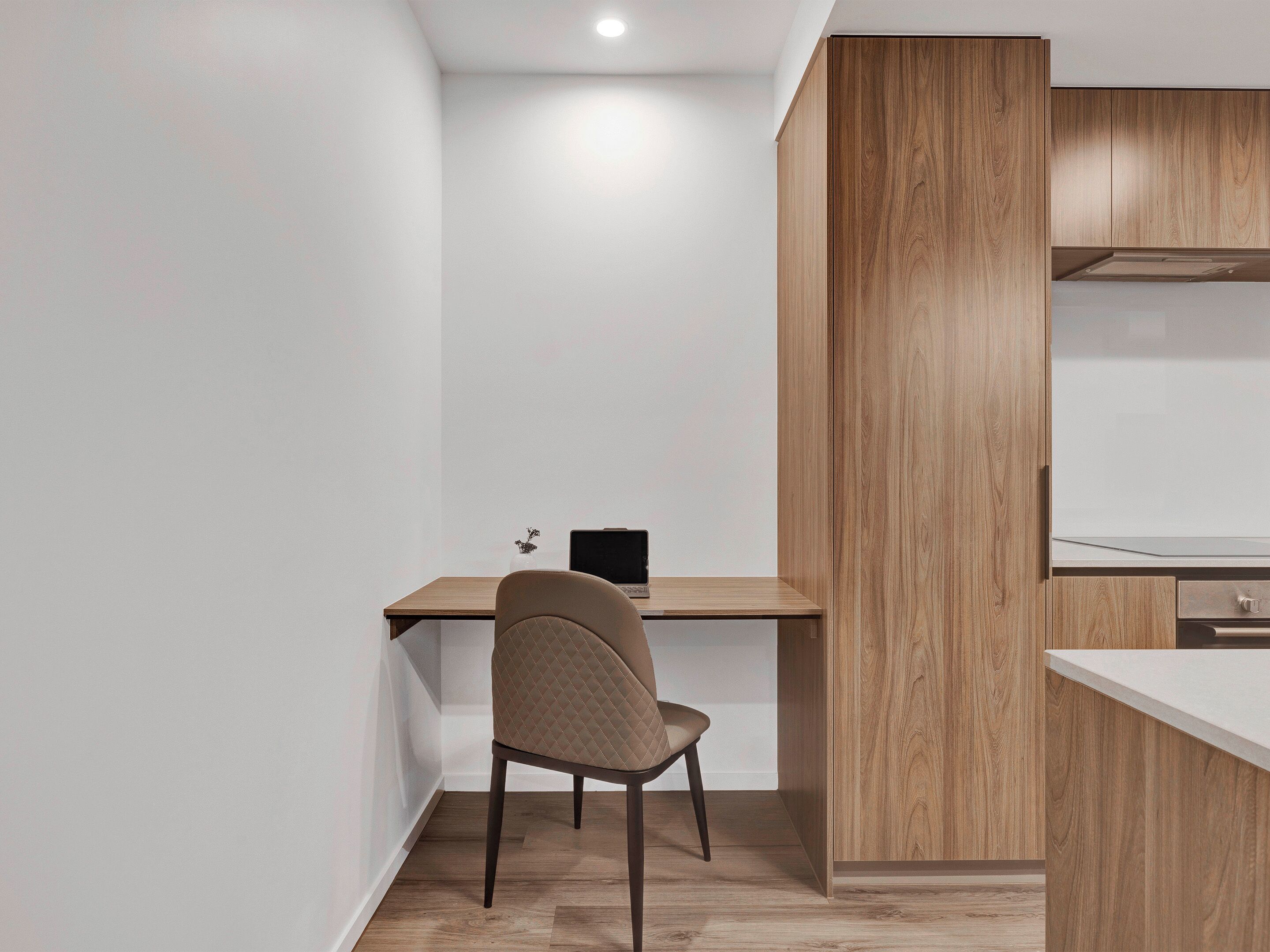 A modern, minimalist room with a wooden desk and chair, a laptop, and a white wall.