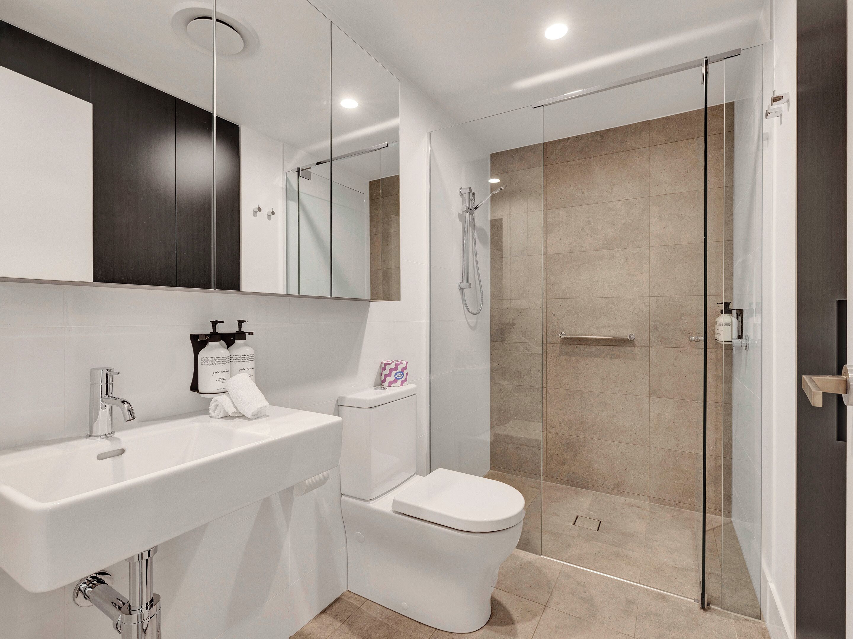 Une salle de bain moderne avec un lavabo blanc, des toilettes et une douche à parois de verre.