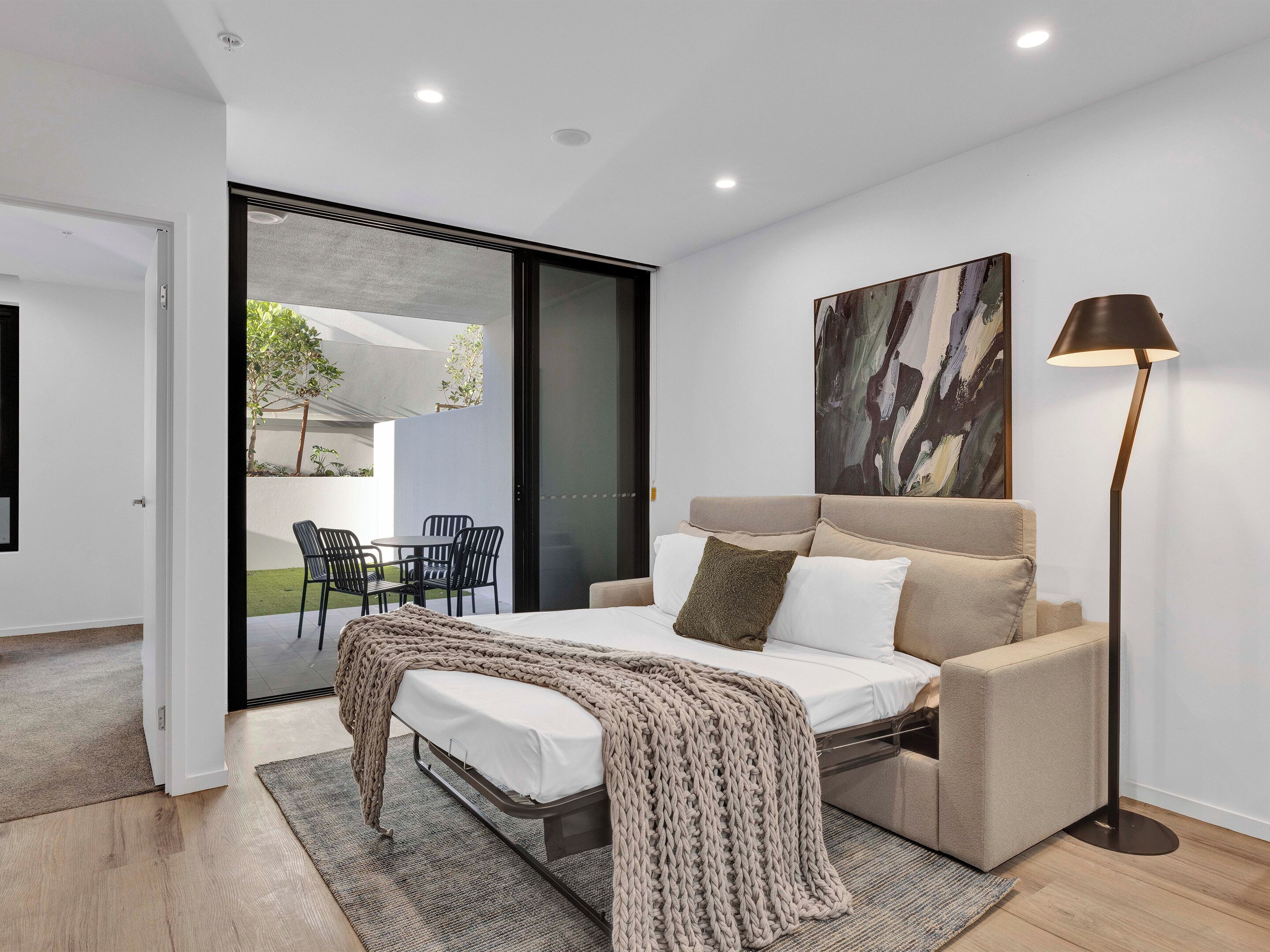 A modern bedroom with a bed, a sofa, a floor lamp, and a painting on the wall.