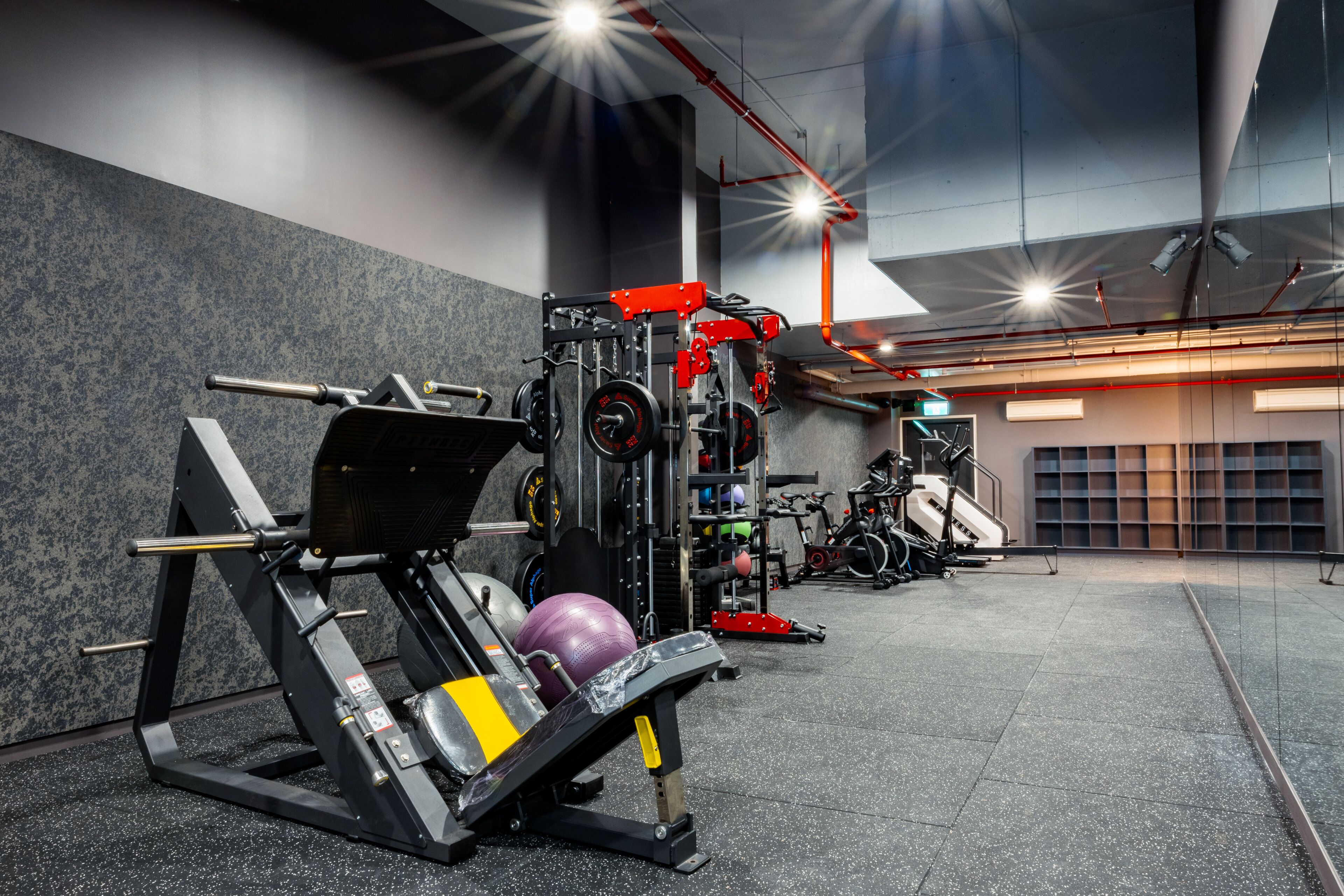 Un gimnasio con diversos equipos de ejercicio, incluyendo una prensa de banca, máquinas de pesas y pesas libres.