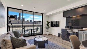 Una sala de estar moderna con un sofá, una mesa de centro y vistas a la ciudad a través de amplios ventanales.
