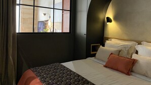 A modern hotel room with a large window, a bed with white linens and a patterned throw, and a unique curved wall design. - Home Chic Home - Les Suites de La Comédie - Suite3 (Montpellier)