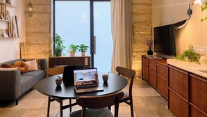 A modern living room with a sofa, a round dining table, and chairs. There is a laptop on the table, a television on the wall, and a window with curtains. - Home Chic Home - Les Suites de La Comédie - Suite3 (Montpellier)