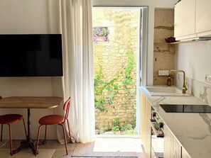 Una cocina moderna con pared de piedra, un televisor de pantalla plana, una zona de comedor con sillas y un lavamanos con grifo dorado.