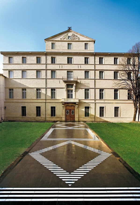 Ein großes, mehrgeschossiges Gebäude mit einer symmetrischen Fassade, einem zentralen Eingang mit einer Tür und einem breiten, gepflasterten Weg, der zum Eingang führt.