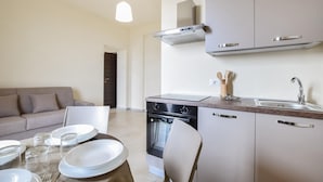 A modern kitchen with a dishwasher, stove, and sink. There is a dining table set with plates and glasses. A sofa and a chair are in the living area. - Beautiful apartment in Patti with WiFi (Patti)