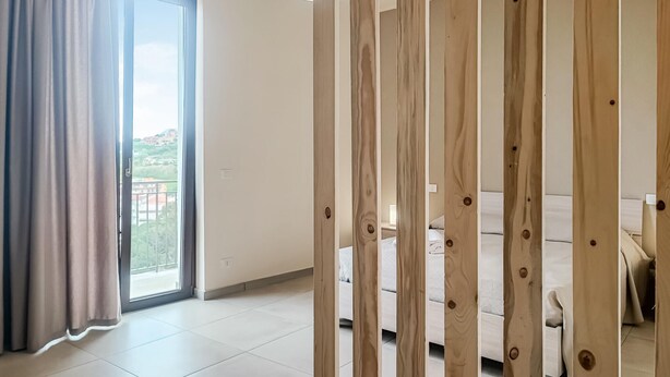 A room with a large sliding glass door leading to a balcony, a white sofa, and wooden slats in the foreground. - Beautiful apartment in Patti with WiFi (Patti)