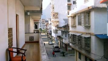 A narrow urban street with residential buildings, a balcony with a chair, and a parked car.